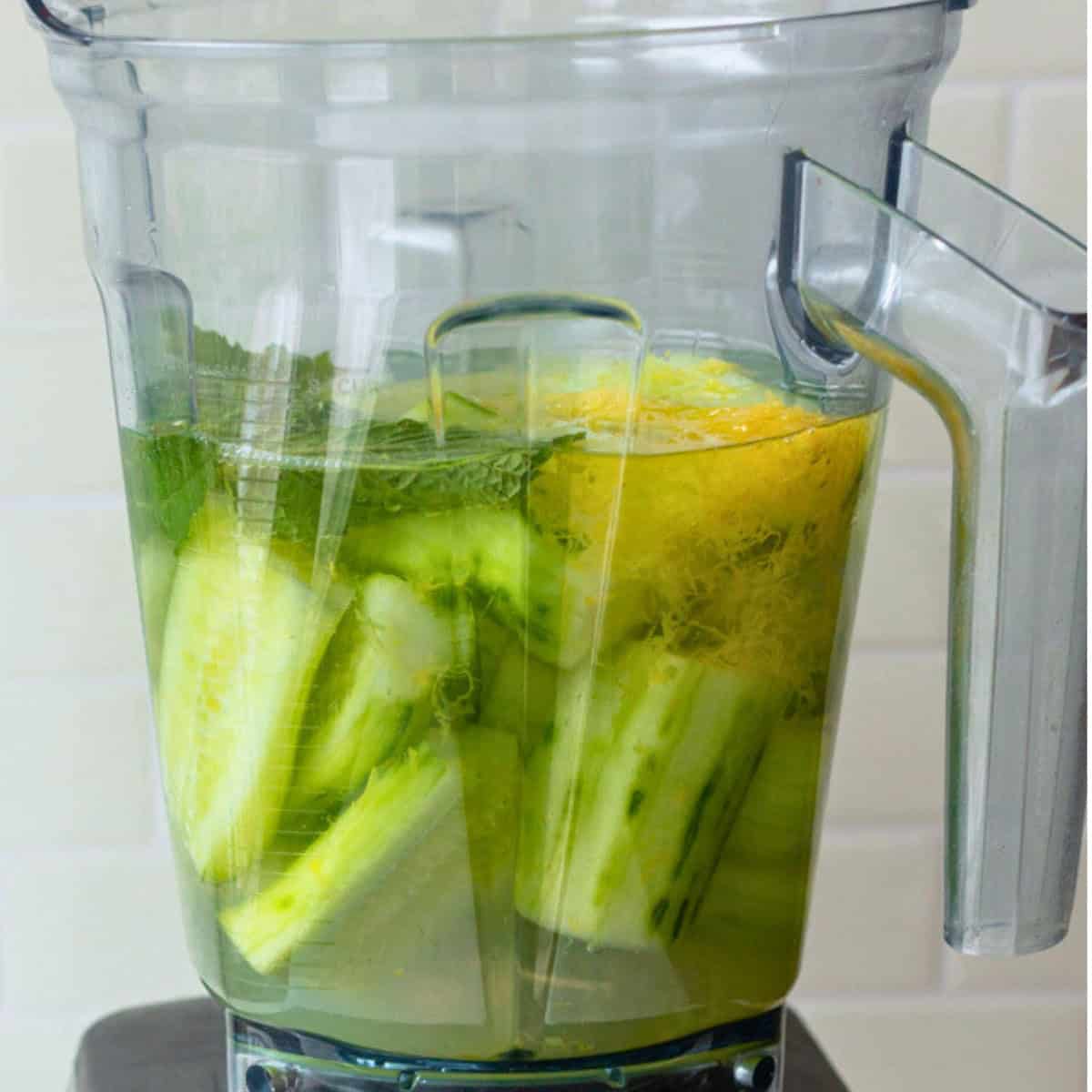 Cucumbers, lemon juice and zest, water, and mint leaves in a blender before blending.