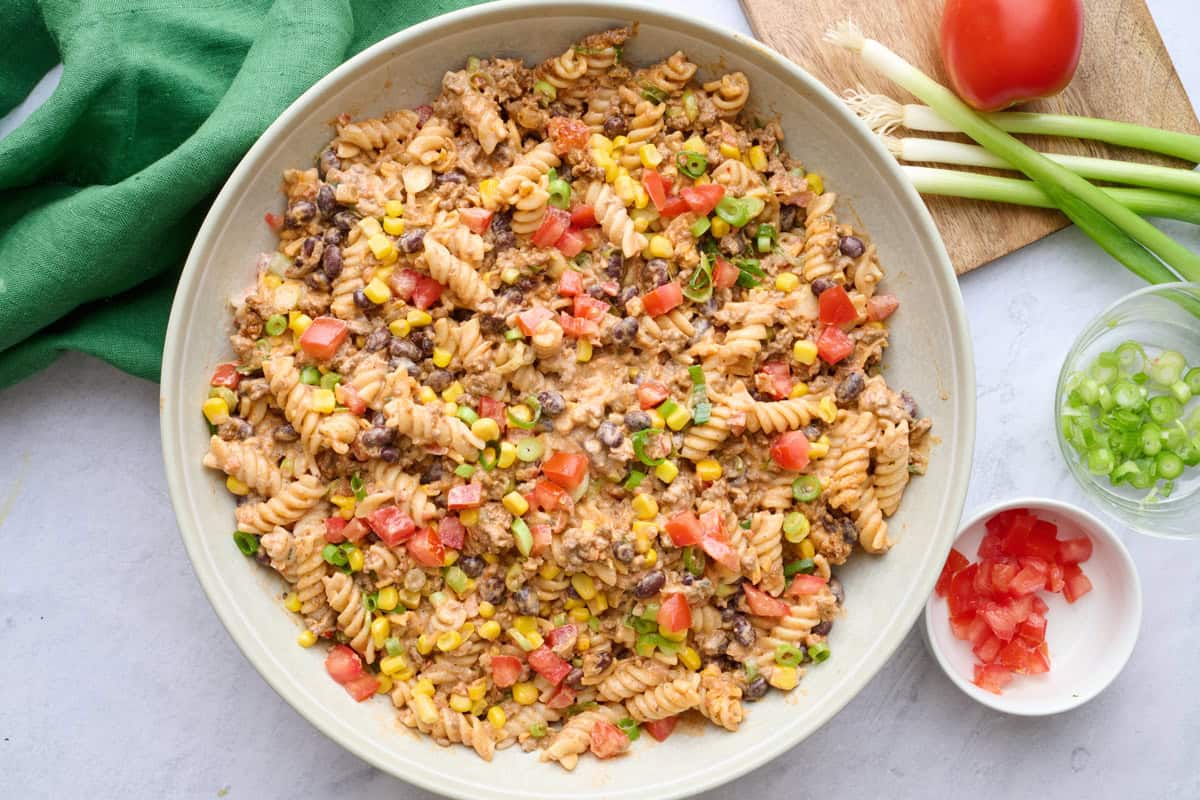 Creamy taco pasta salad recipe with ground beef, beans, and cheese in a serving bowl.