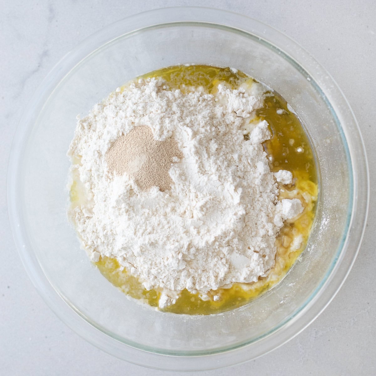 Flour, sugar, oil, water, and yeast in a bowl before combining to make meat pie dough.