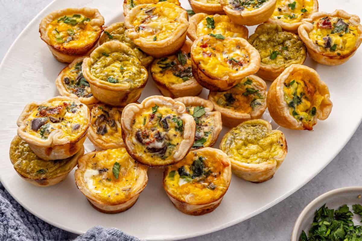 Mini quiches on a platter garnished with chopped parsley.