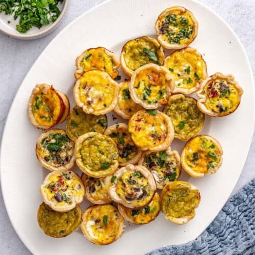 Mini quiches on a platter garnished with chopped parsley.