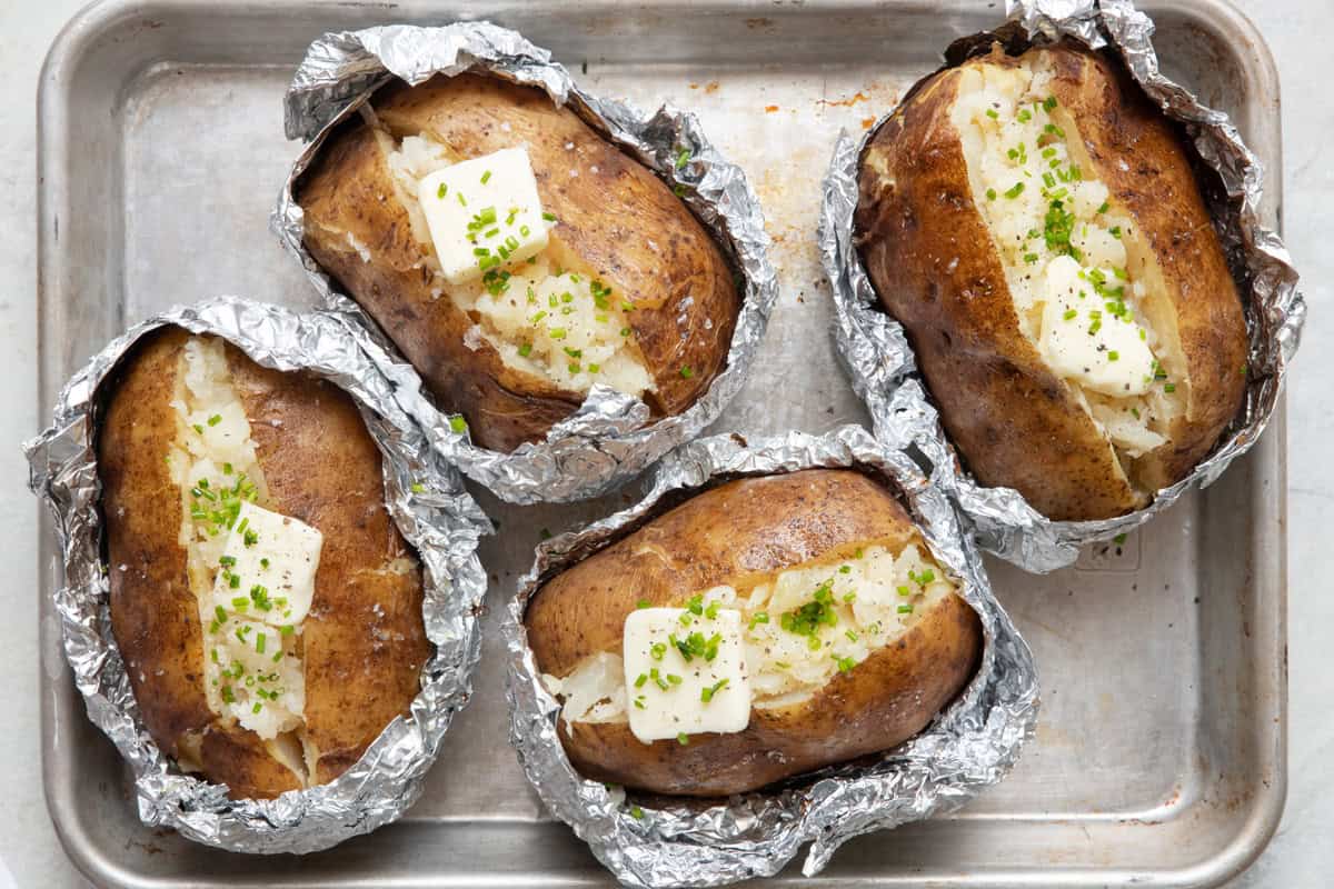 Grilled baked potatoes cut open with butter and chives on top.