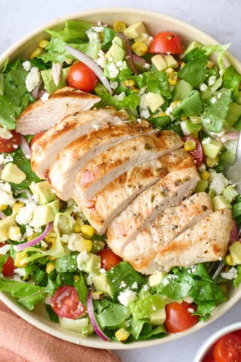2 bowls of grilled chicken salad with extra fresh ingredients around.