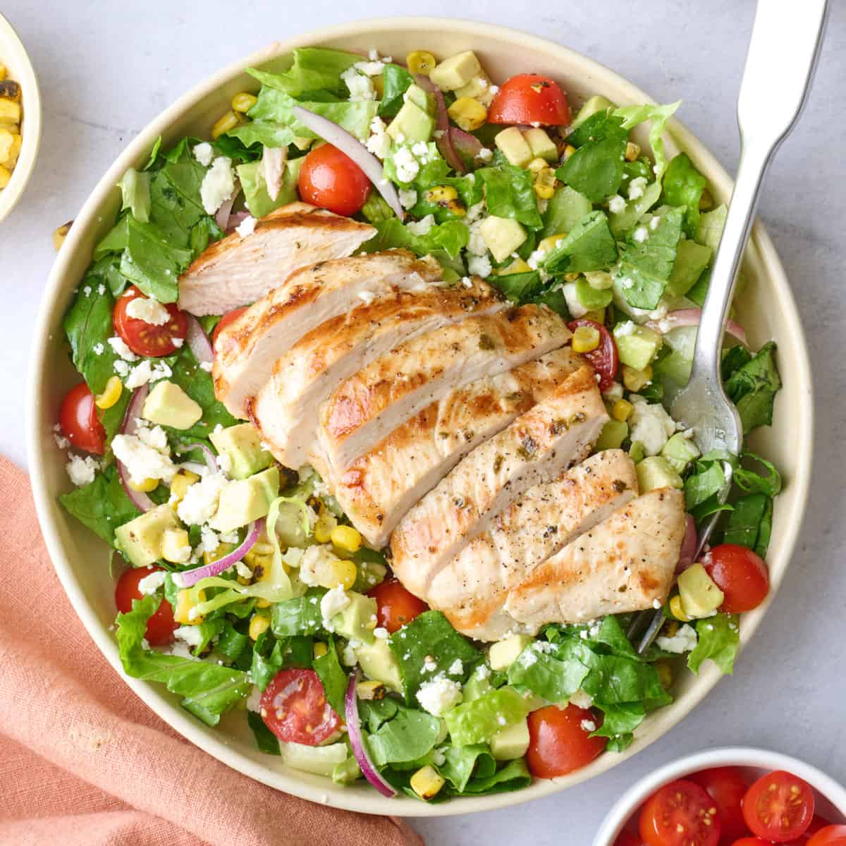 2 bowls of grilled chicken salad with extra fresh ingredients around.