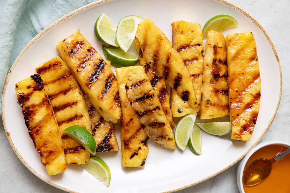 Grilled pineapple wedges on a platter drizzled with honey and served with lime.