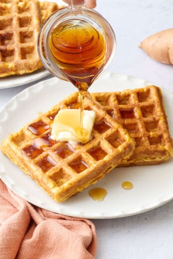Syrup being poured over a plate of sweet potato waffles.