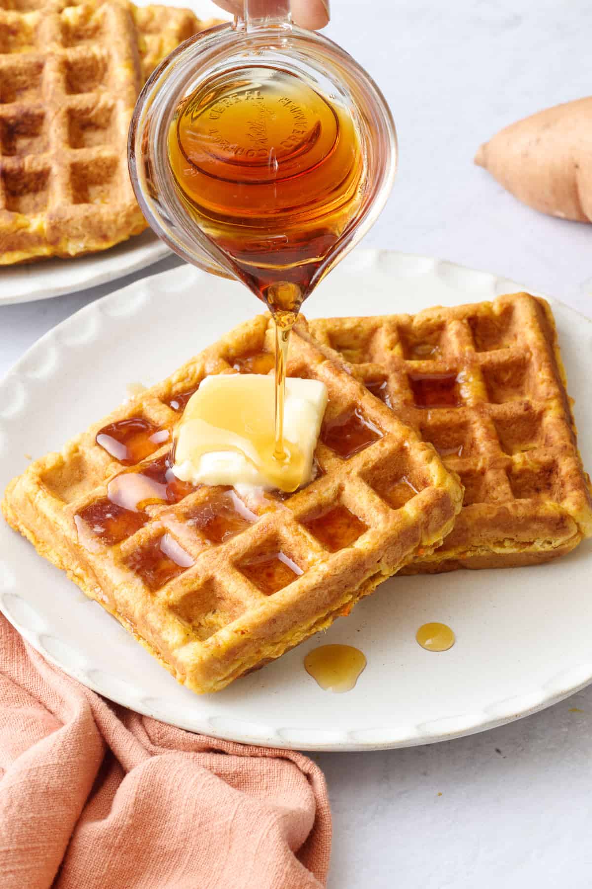 Syrup being poured over a plate of sweet potato waffles.