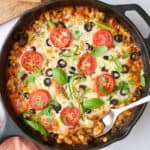 Pizza beans garnished with fresh basil with crusty bread nearby, serving removed with spoon dipped inside.